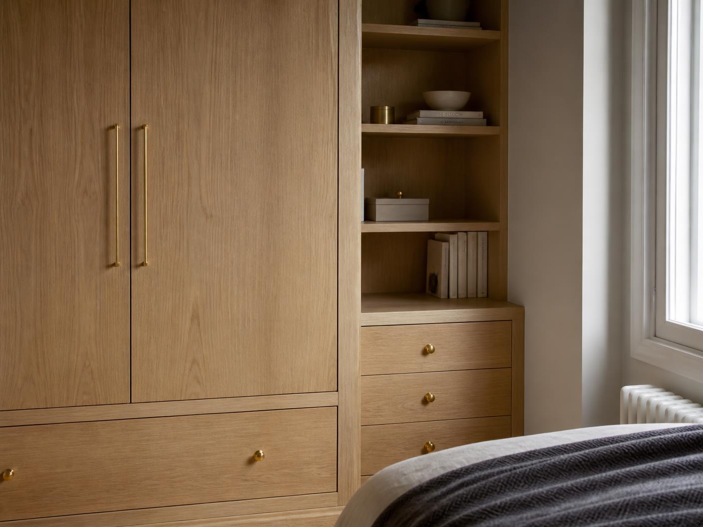 Bespoke oak fitted wardrobe and alcove shelving with brass hardware in a London bedroom