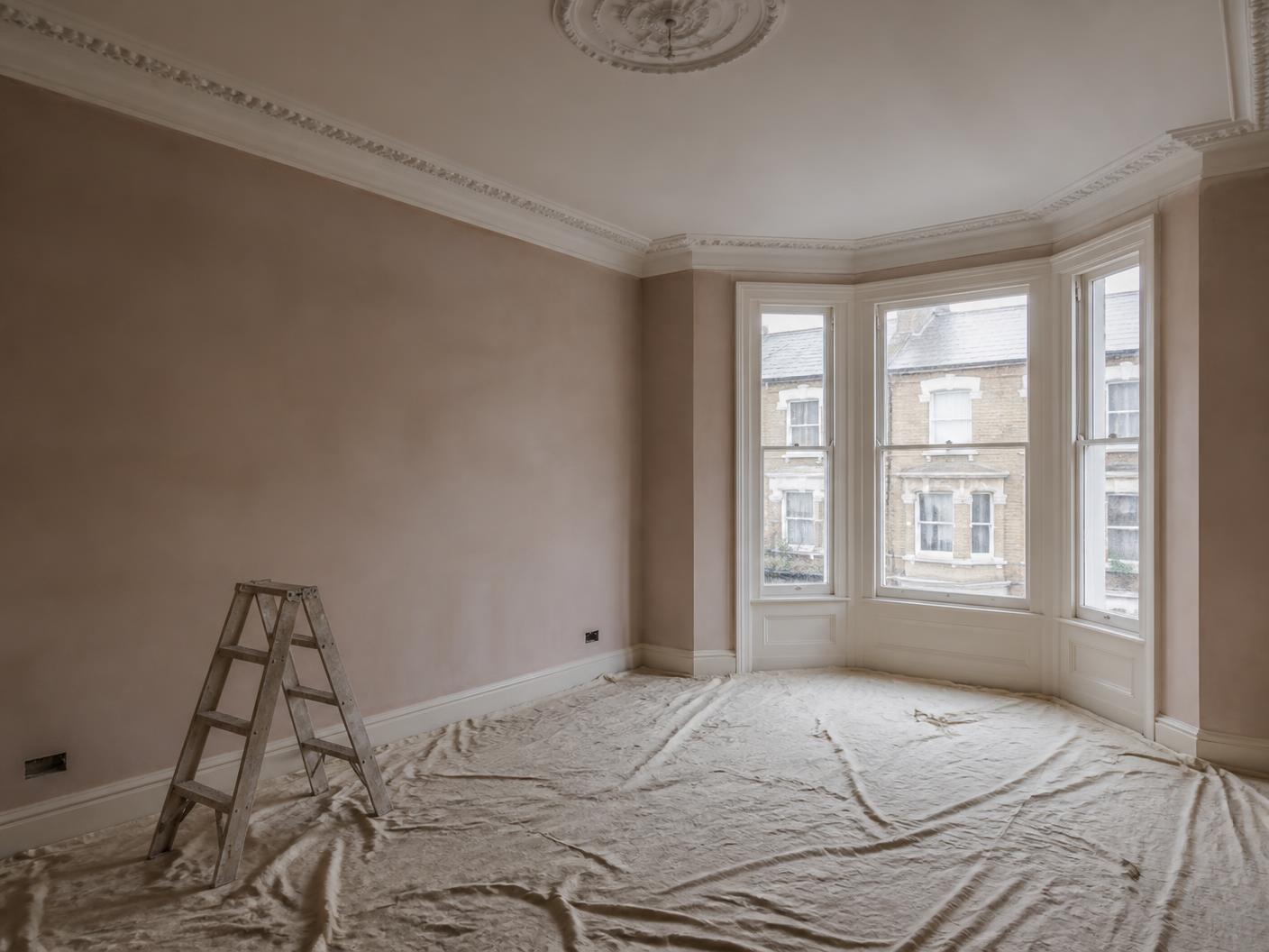 Freshly skimmed plaster walls in an empty Victorian London room with dust sheets